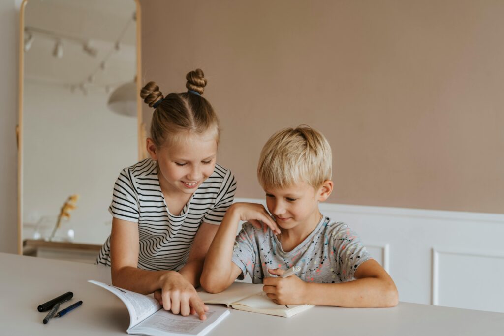 Two kids studying together at home, focusing on a book in a calm, indoor setting.